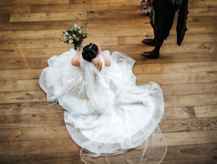 View from above of bride holding bouquet and sitting on wooden floor